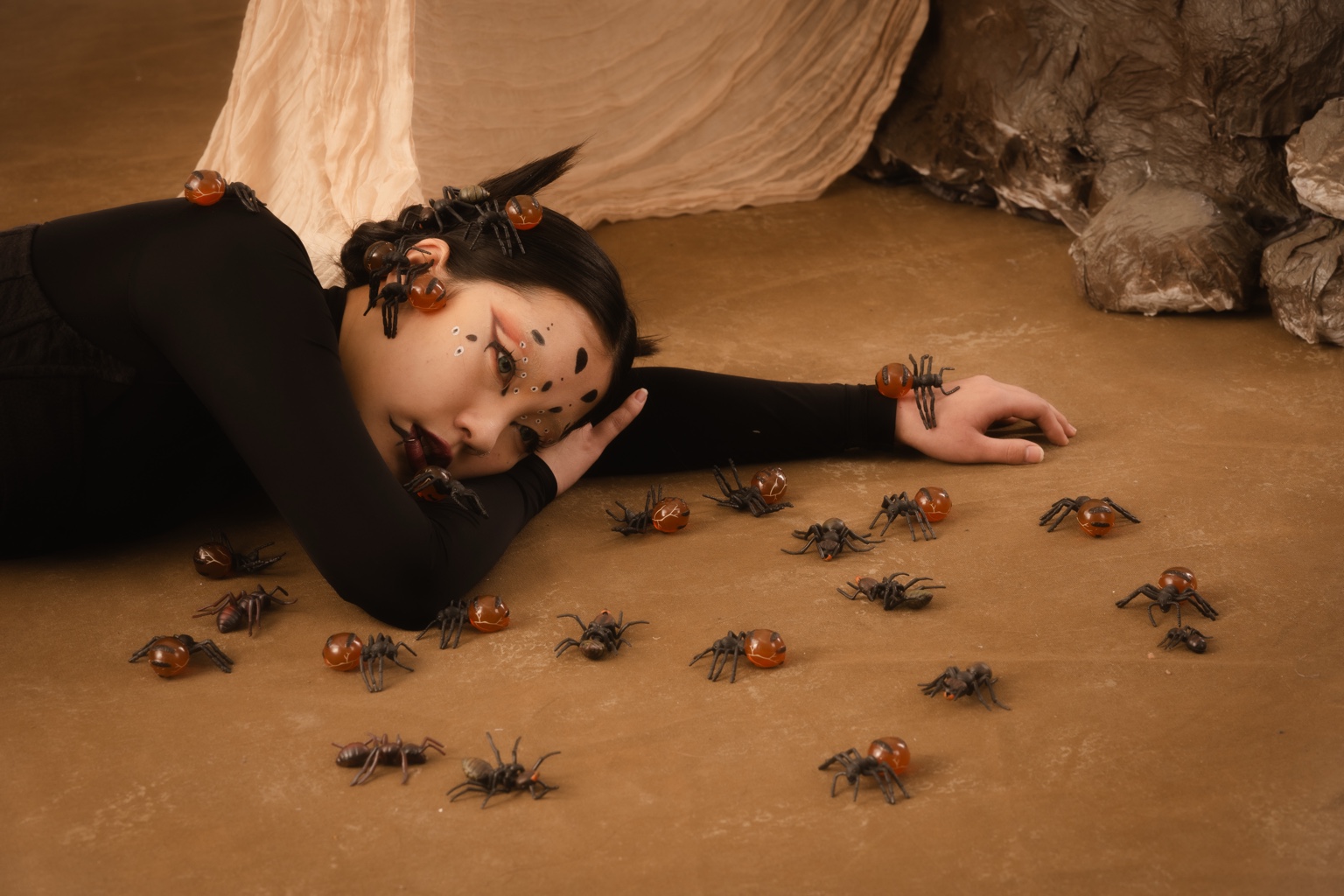 Model reclining among amber insect props, with draped fabric and sculptural set pieces